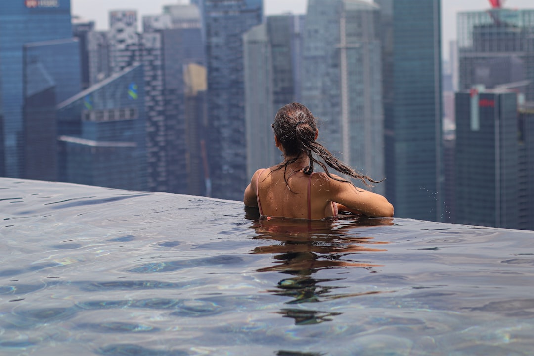 A woman relaxing by an infinity pool during a luxury staycation in Singapore with the city skyline in the background
