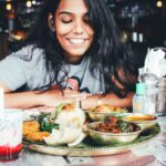 A Singaporean expat woman shares a meal at an outdoor hawker-style food stall, connecting community through food abroad