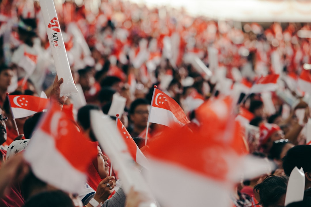 A crowd of Singaporeans cheering together inside a stadium during the National Day Parade, dressed in red and white