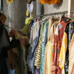 A woman carefully browsing a clothing rack at one of Singapore's secondhand platforms, looking for preloved fashion finds.